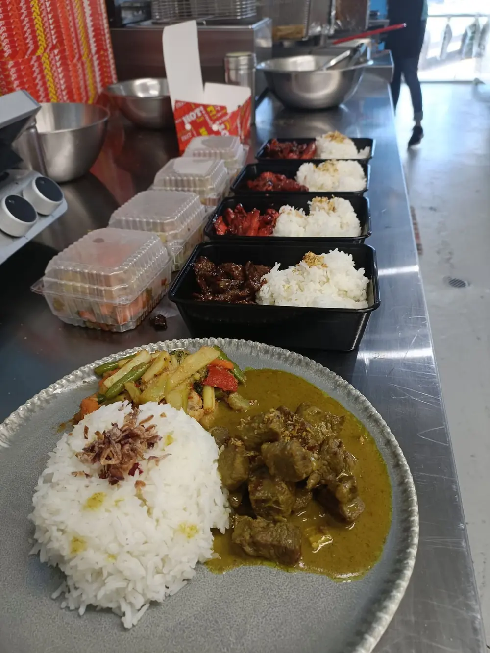 Multiple takeaway meal boxes lined up on a preparation bench
