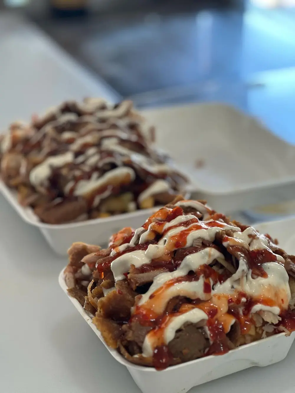 Two loaded snack packs topped with meat and sauces