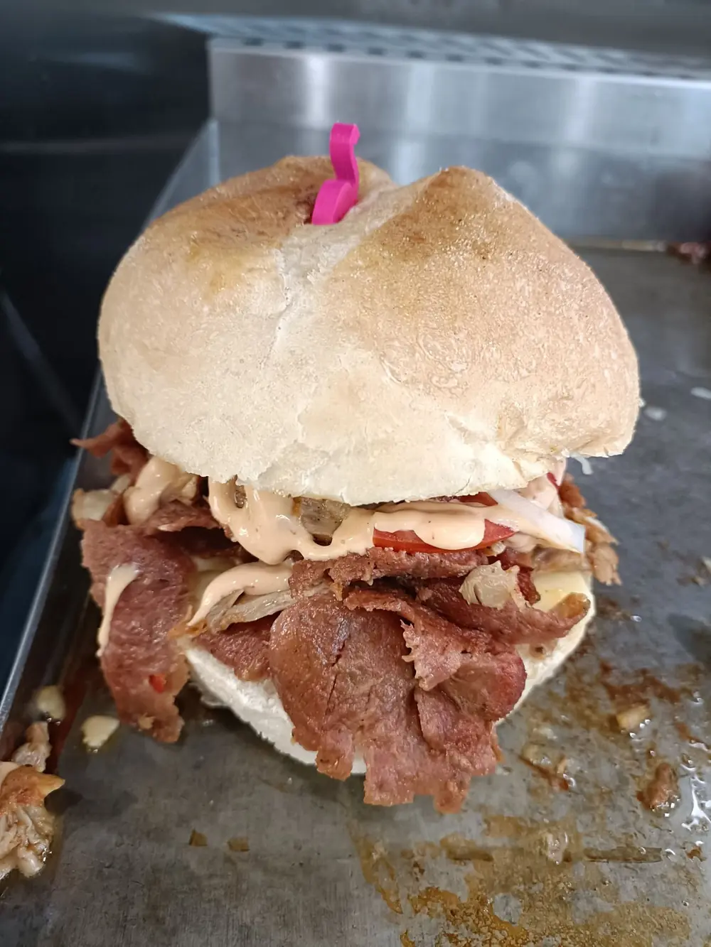 Large meat-filled burger with sauce on a preparation bench