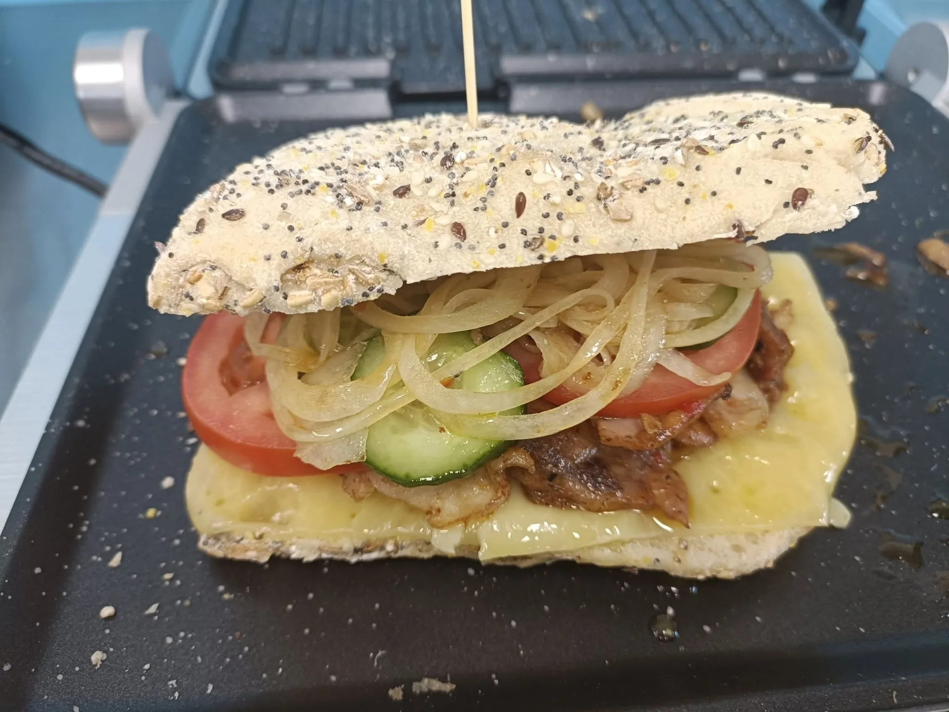Filled bread with meat, cheese, tomato, cucumber and onion on a grill